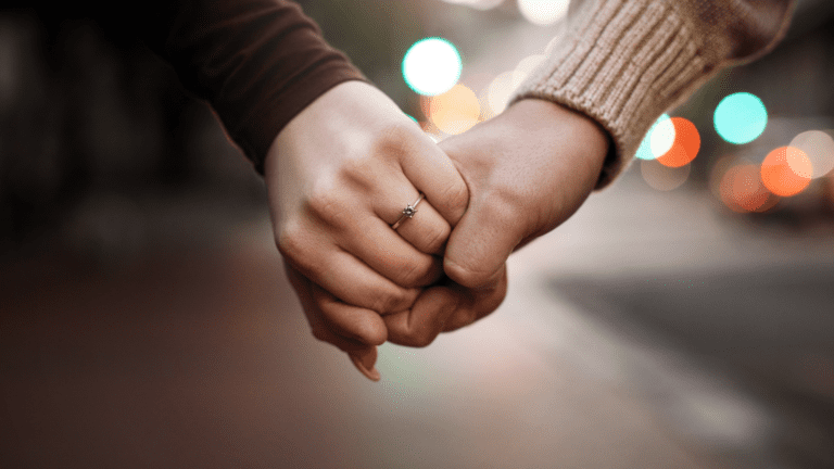 Couple Holding Hands With Engagement Ring lights in background